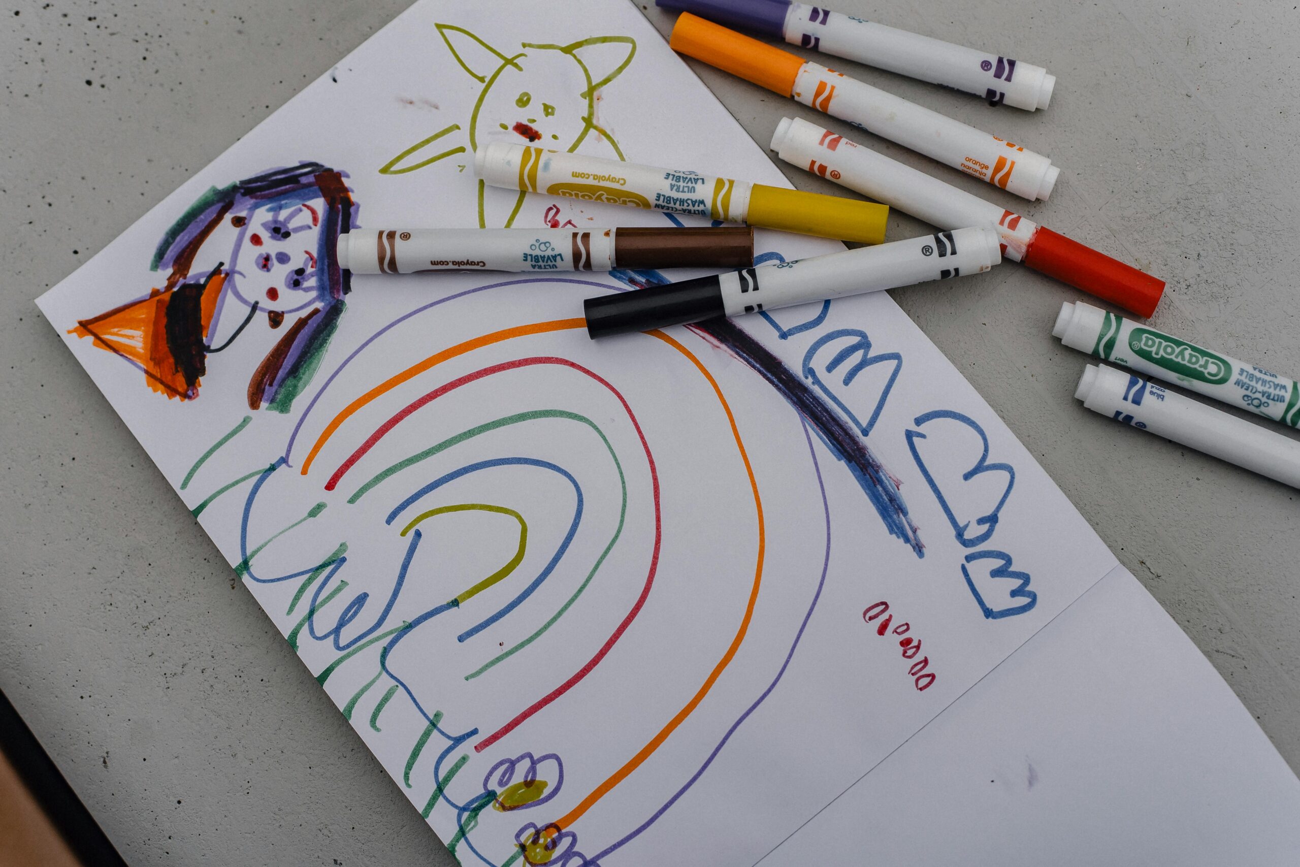 A child's vibrant drawing with markers featuring a rainbow and doodles on white paper.
