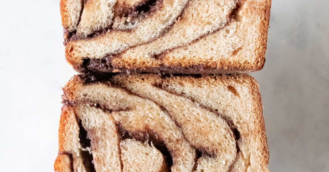 Close-up of a hand holding delicious chocolate babka slices with swirled patterns.